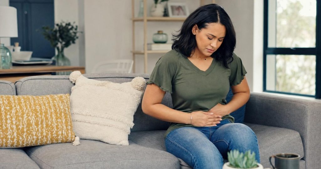 Adult at home holding abdomen with mild stomach discomfort - SemaLiving guide to Ozempic stomach pain